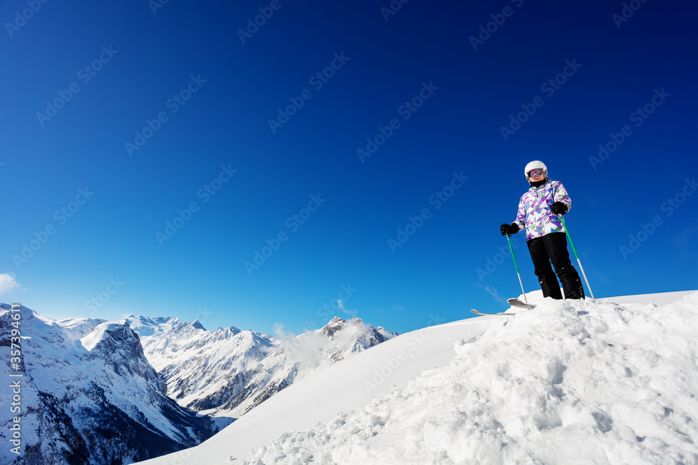 自信酷炫的滑雪女孩穿着运动装备站在雪堆上，俯瞰广阔的山脉全景