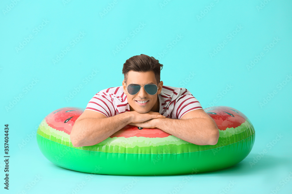 Young man with inflatable ring on color background