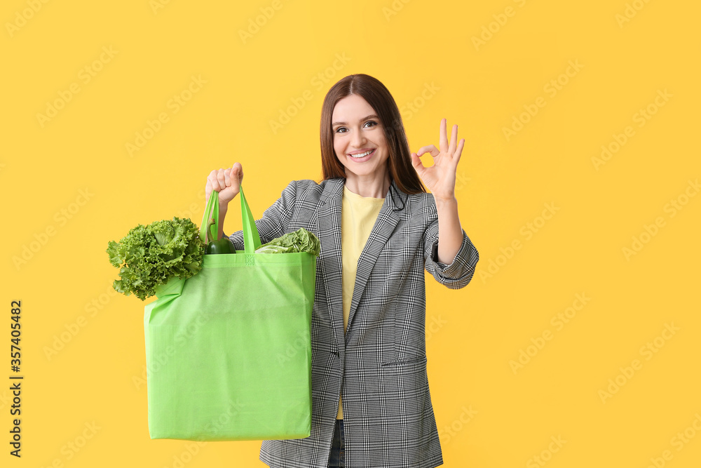 Young woman with food in bag showing OK gesture on color background