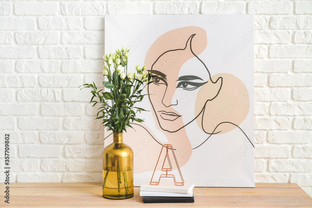 Vase with beautiful flowers, books and picture near white brick wall