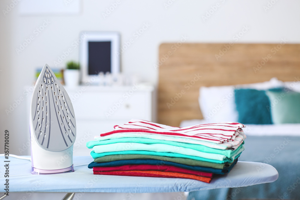 Stack of clean clothes on ironing board in room