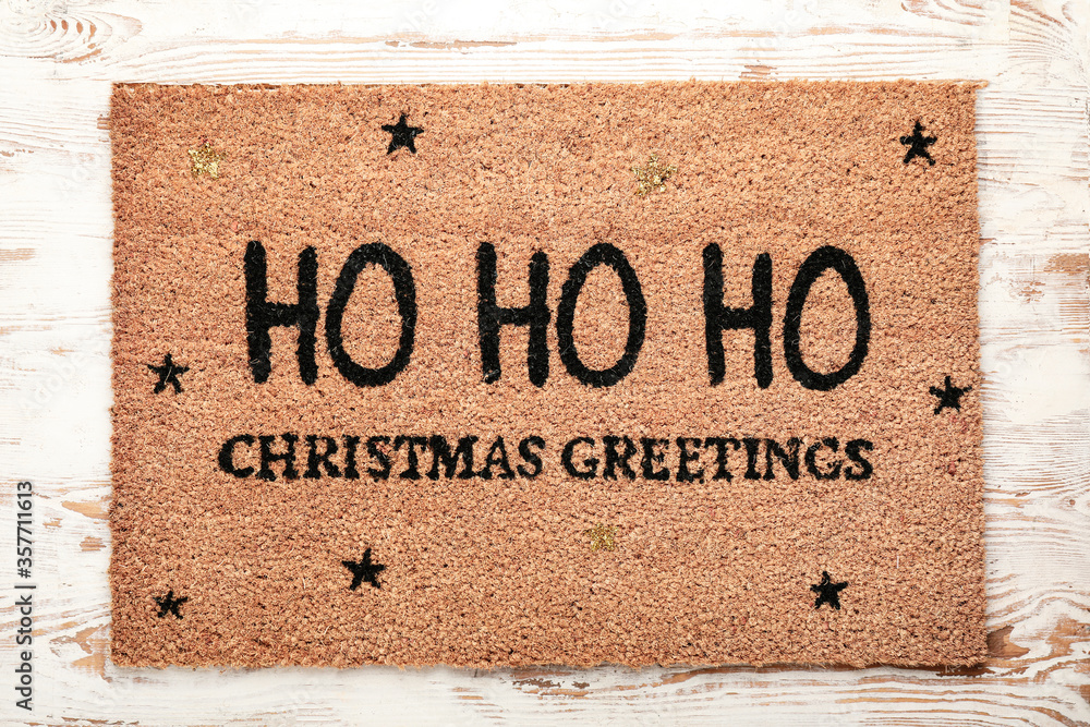 Door mat with Christmas greeting on wooden background