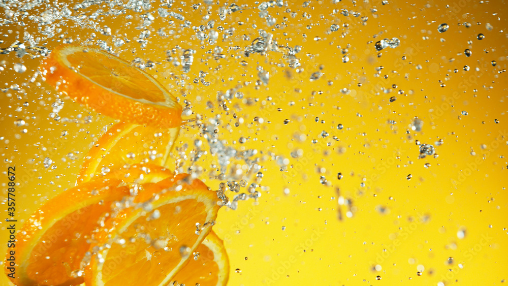 Freeze motion of flying orange pieces with water splashes. Studio shot of fresh summer beverage on s