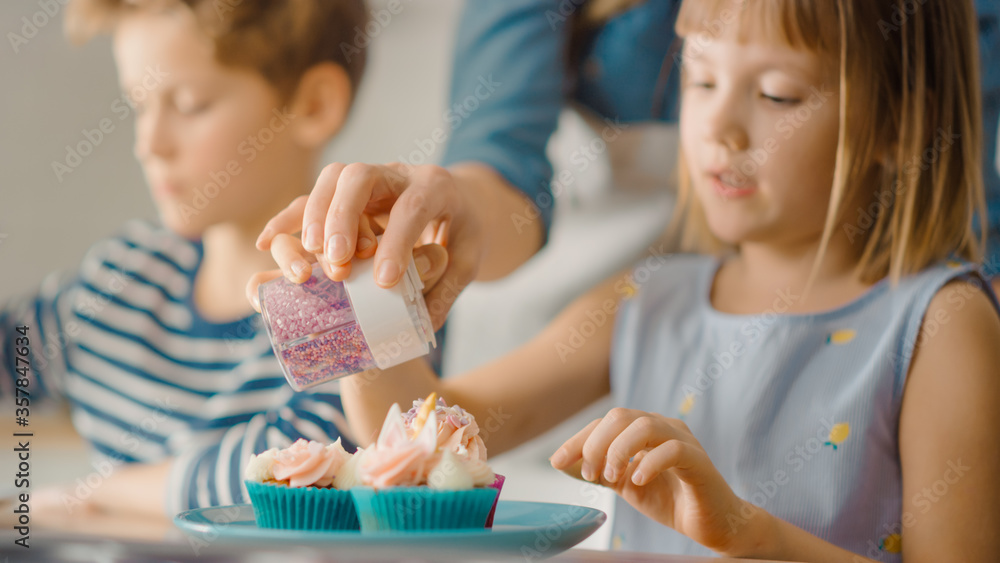 In the Kitchen: Portrait of the Cute Little Daughter Sprinkling Funfetti on Creamy Cupcakes Frosting