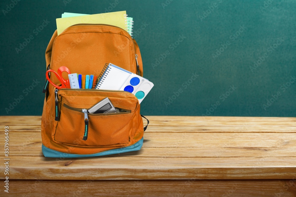 Classic school backpack with colorful school supplies and books on the desk.