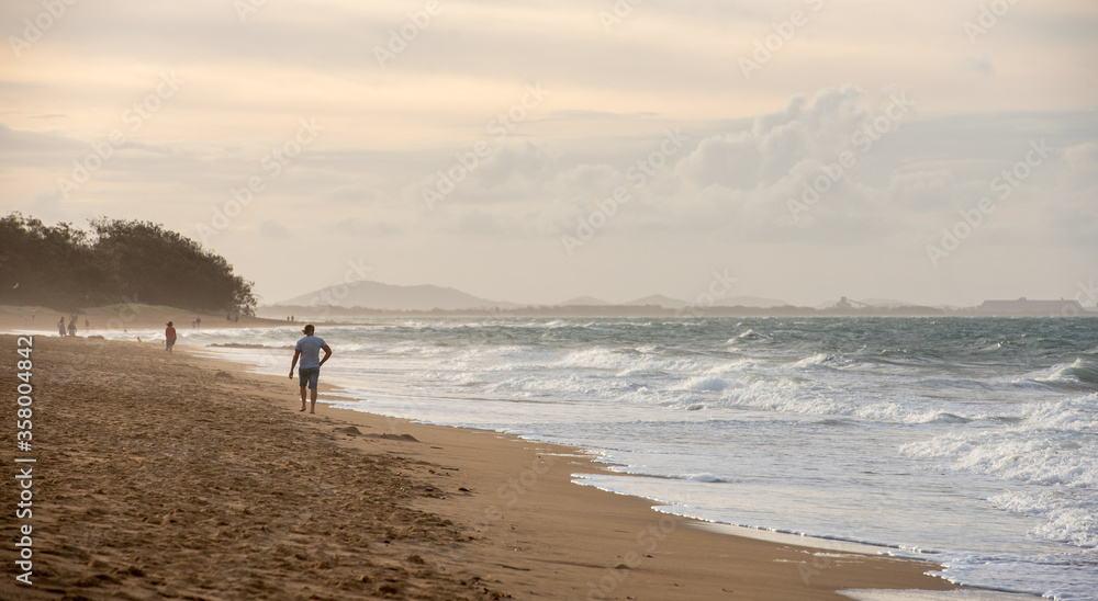 Man walking along Tannum Sands beach with industry in the background, Gladstone Region, Queensland