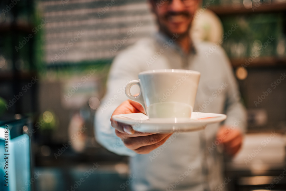 Barista giving cup of coffee toward camera, close-up, copy space.