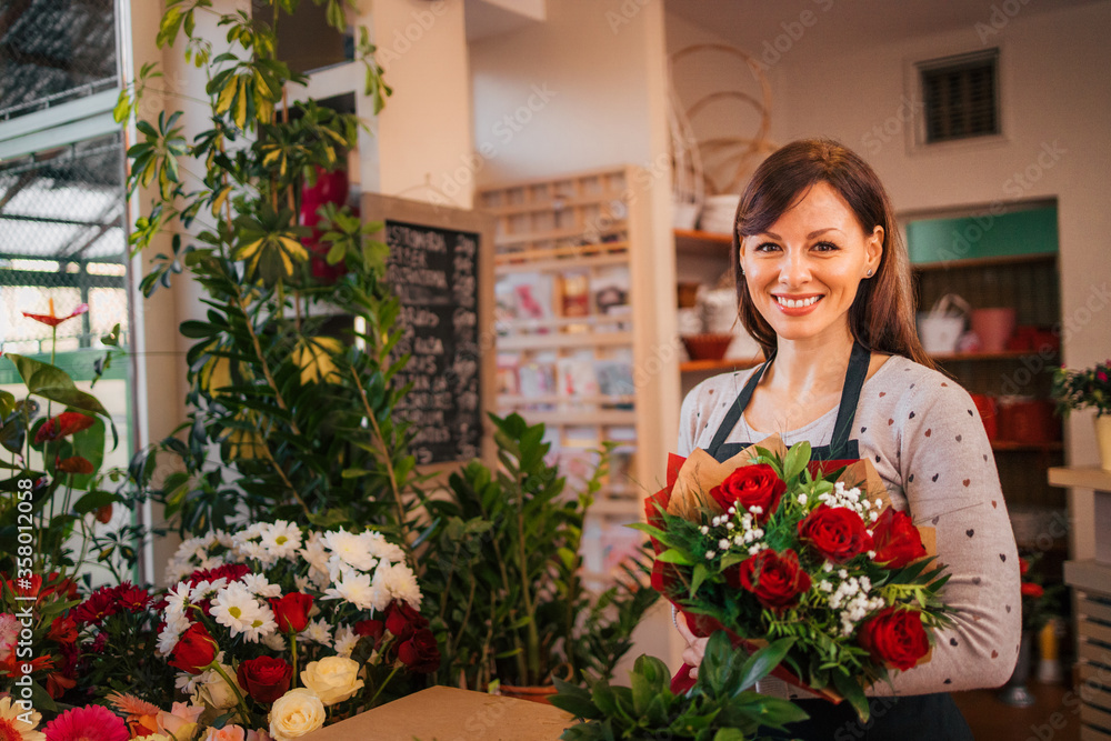 Small business. Portrait of a smiling florist holding bouquet while surrounded with beautiful flower