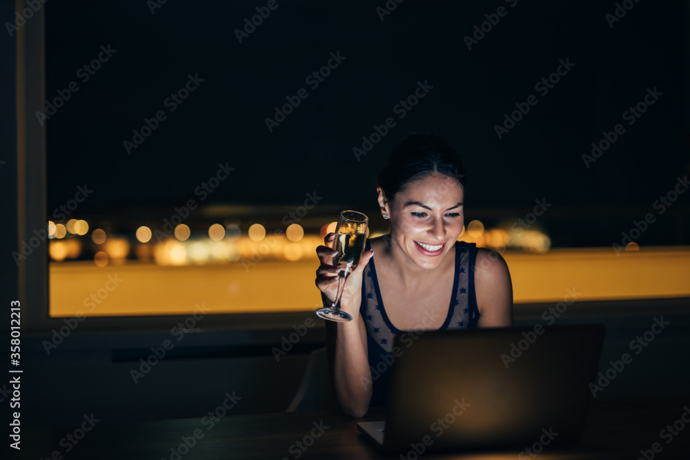 Beautiful woman using laptop at night and having a drink, portrait.