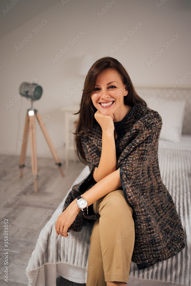 Beautiful woman sitting on the bed and smiling at camera, portrait.