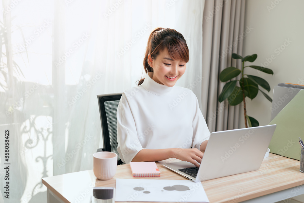 Cheerful young Asian woman working at home with computer