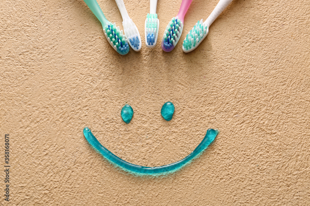 Toothbrushes and smile made of paste on color background