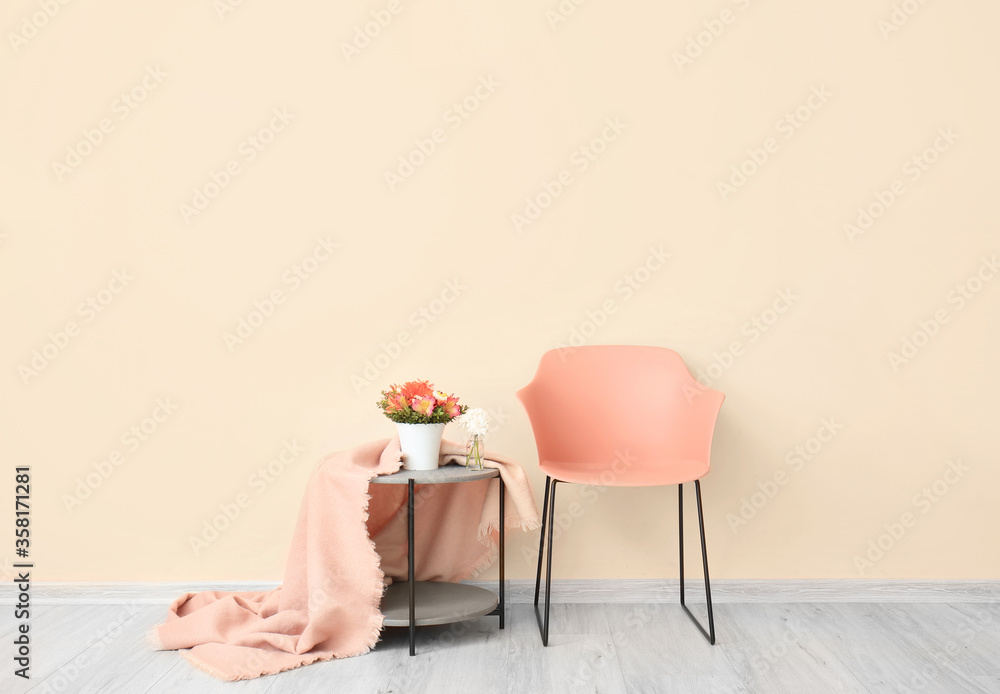 Armchair and table with flowers and plaid near color wall in living room