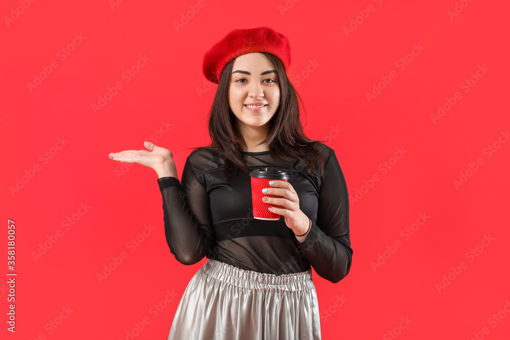 Beautiful young woman with cup of coffee showing something on color background