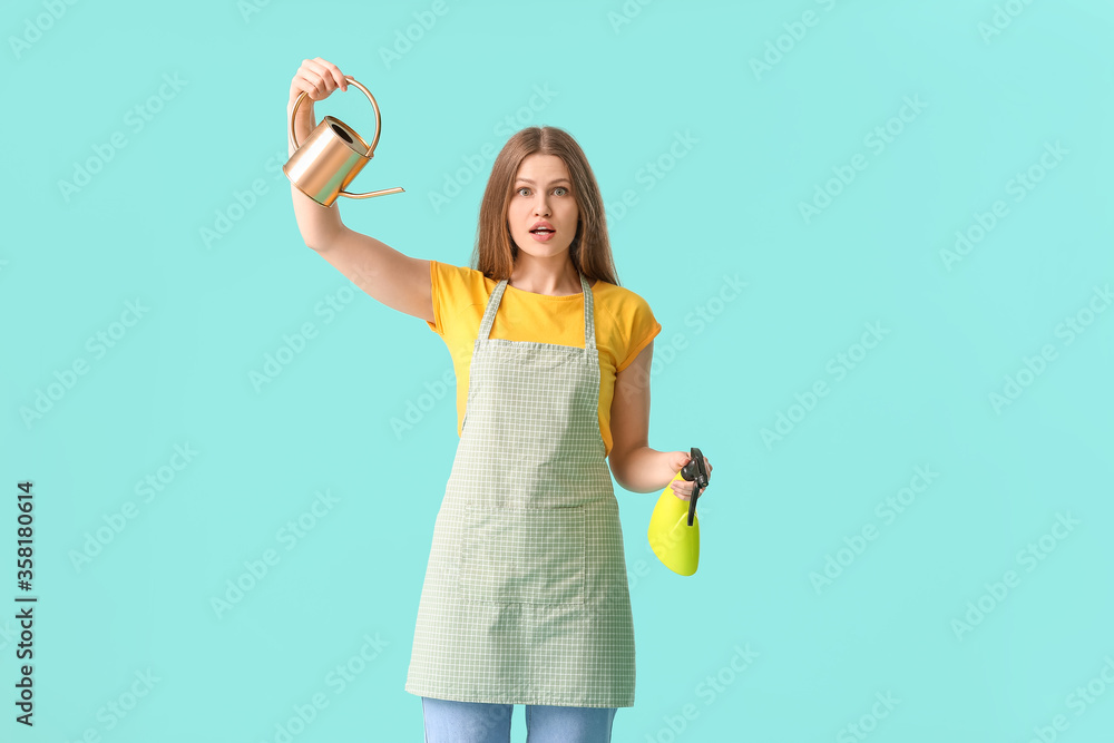 Surprised young woman with watering can and water sprayer on color background