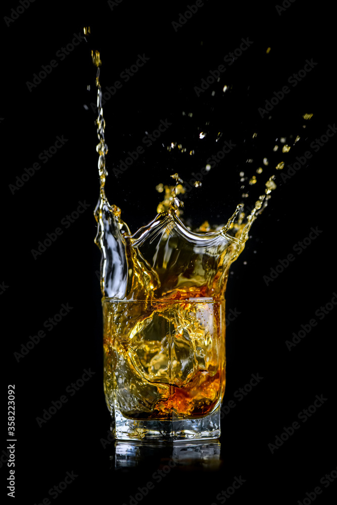 Splashing of whiskey out of glass isolated on black