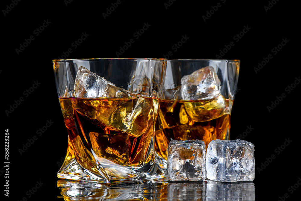 Glass of whiskey with cube ice on black background