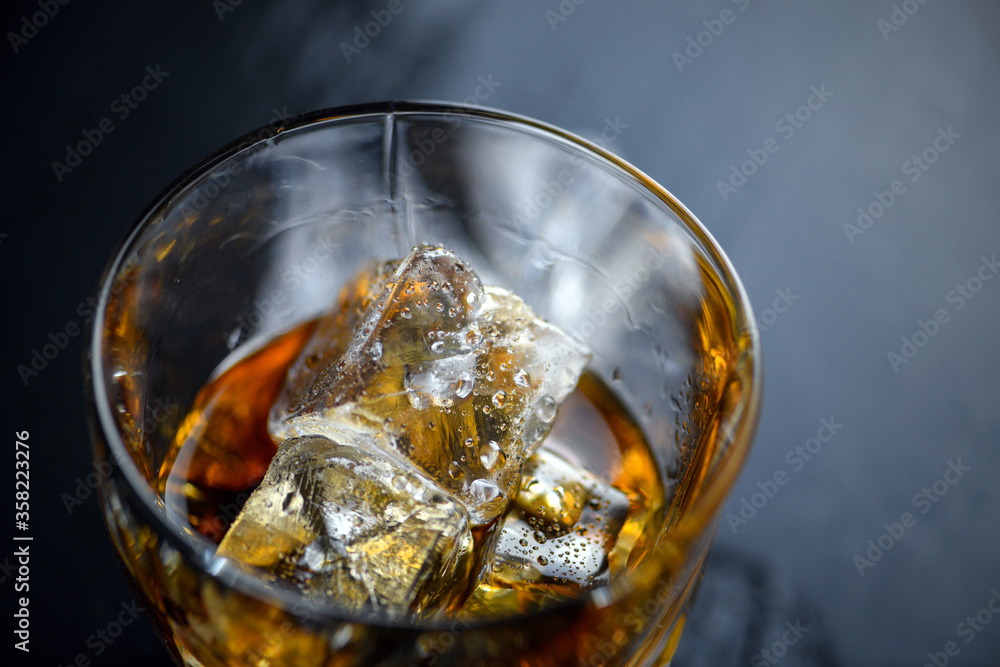 Glass of whiskey with cube ice on black background