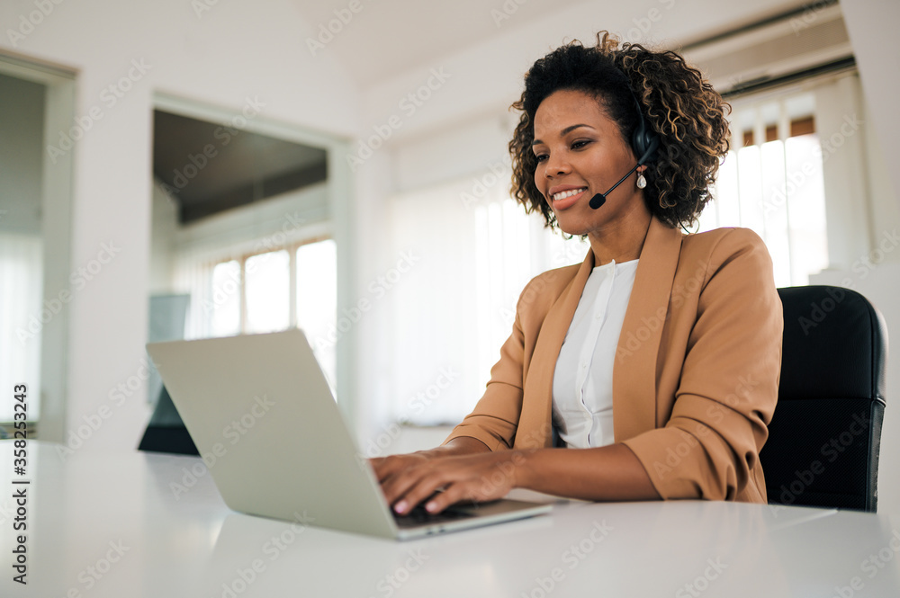 Portrait of a beautiful customer support operator with headset working on laptop.