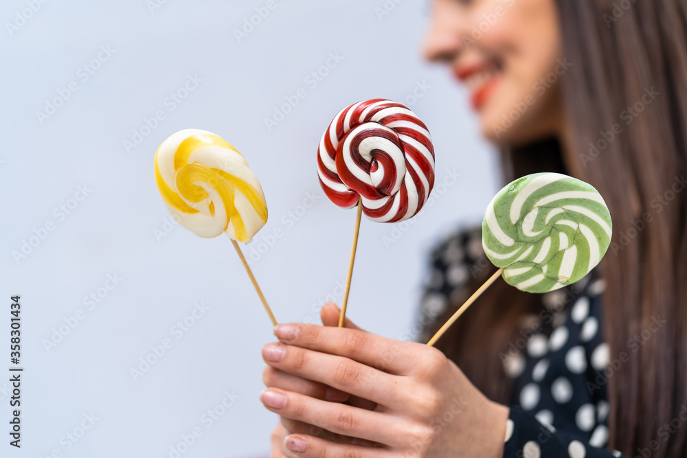 Young beauty in dotted shirt with three lollipops in hands. Cheerful lady with candies over white ba