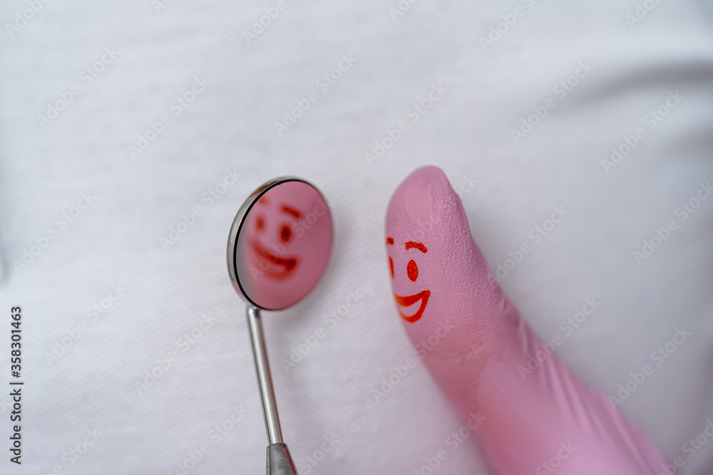 Finger in pink gloves with red smile on it. Looking to the dentist`s mirror.