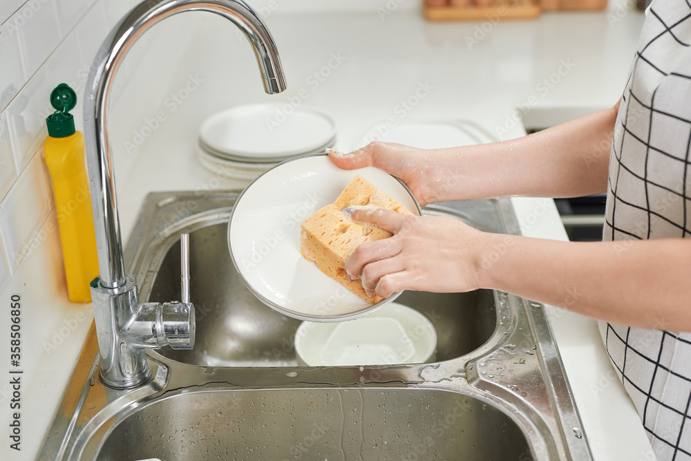 Cropped image of attractive young woman is washing dishes while doing cleaning at home