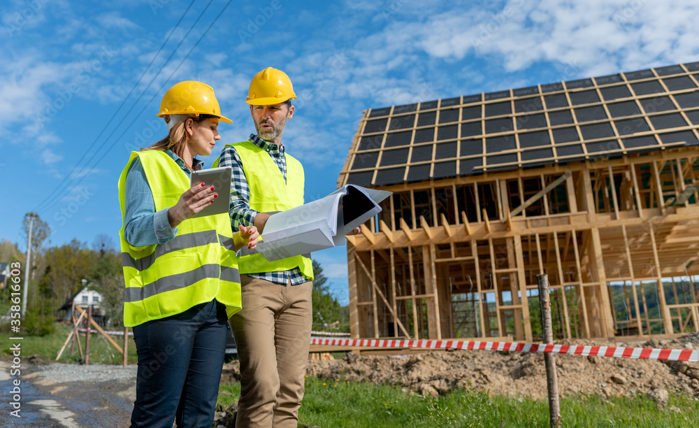 Engineers working on construction site holding blueprints of wood frame house