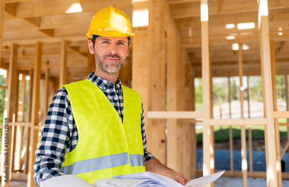 Construction engineer or architect with blueprints visiting building site of wood frame house