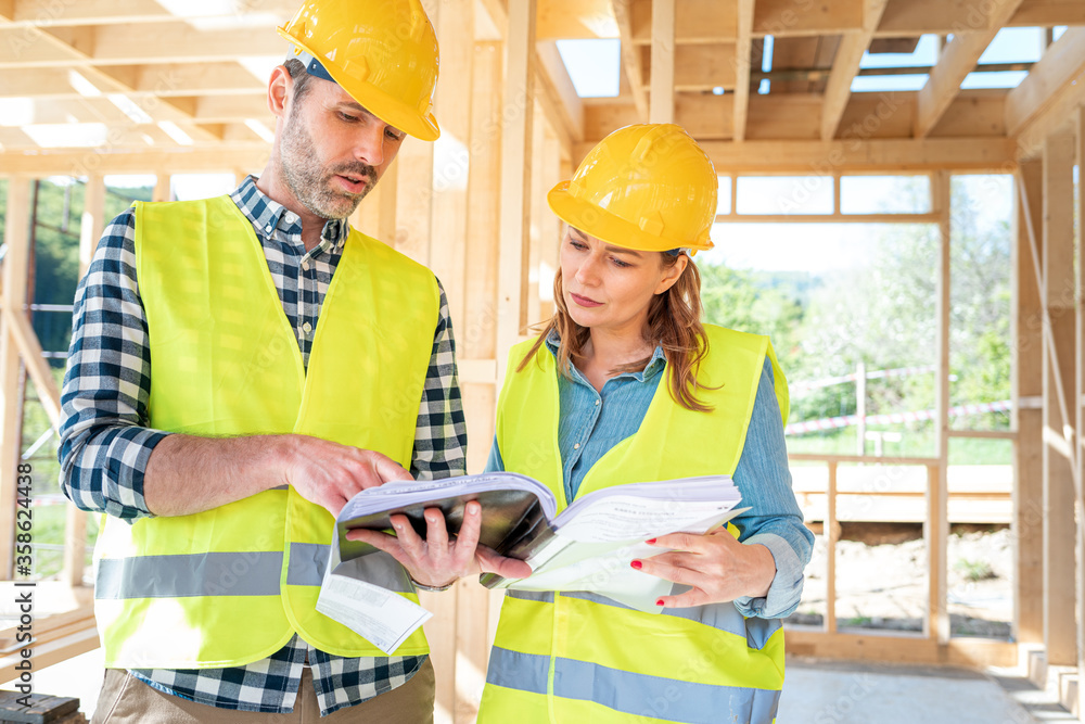 Construction engineer and architect consult plans on building site of wood framing house under const