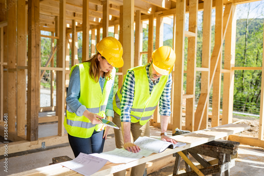 Construction engineer and architect consult plans on building site of wood framing house under const