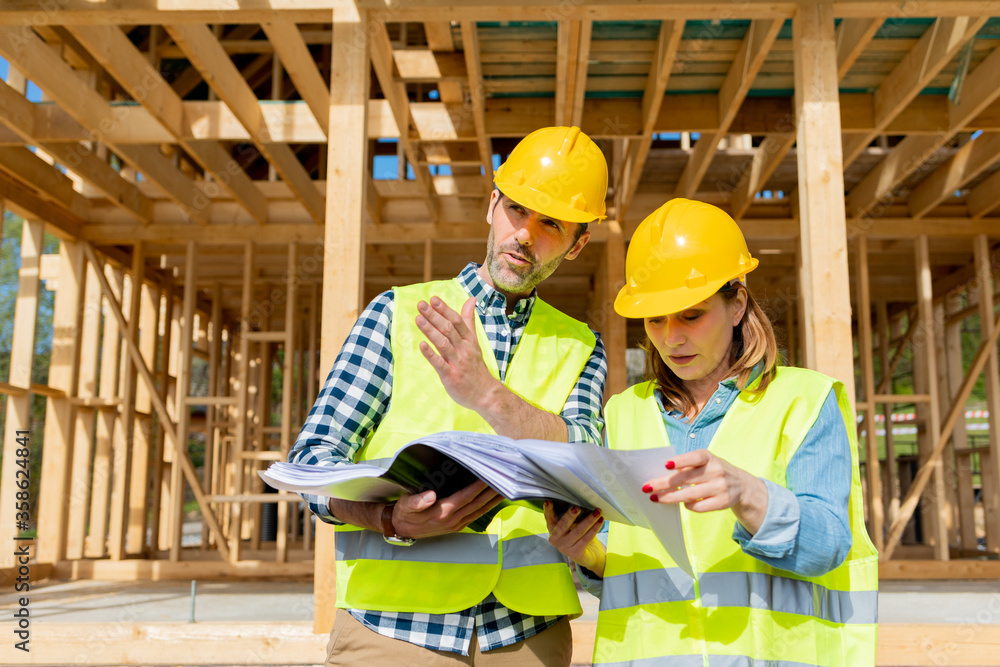 Construction engineer and architect consult plans on building site of wood framing house under const