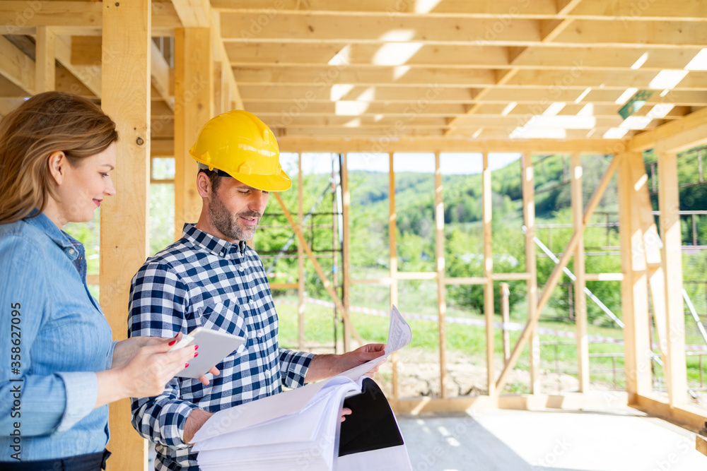 Architect or engineer with blueprints meeting with owner of building house on construction site