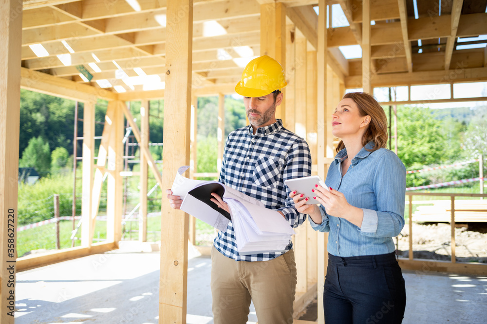 Architect or engineer with blueprints meeting with owner of building house on construction site