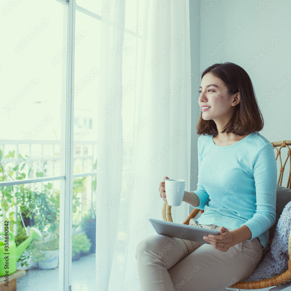 young Asian woman sitting behind the window and drinking coffee in the morning.