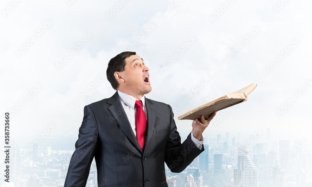 Surprised businessman holding open old book