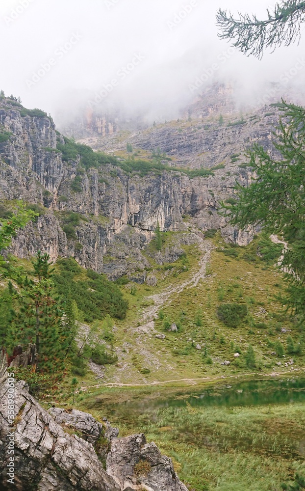 Bright gray-green summer landscape of the Dolomites of Italy. In the foreground is a large stone and