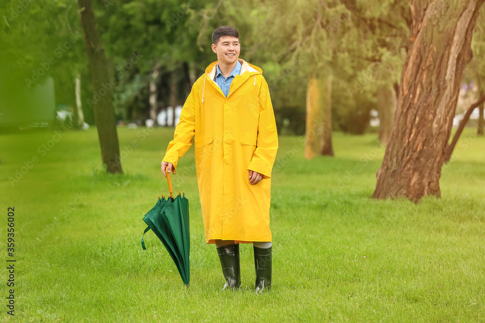 亚洲年轻男子在公园里打着雨伞，穿着雨衣