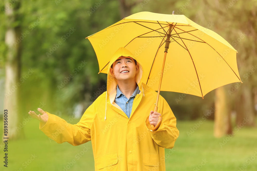 亚洲年轻男子在公园里打着雨伞，穿着雨衣