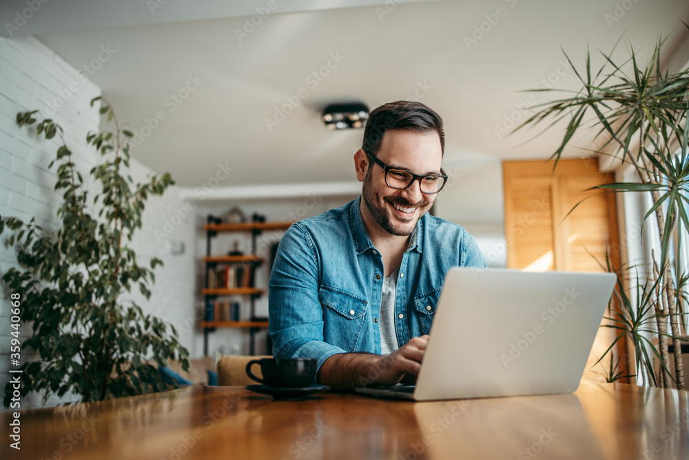 Portrait of a cheerful man using laptop while sitting at wooden table.