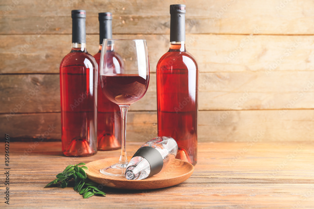 Aerator with glass and bottles of wine on wooden background