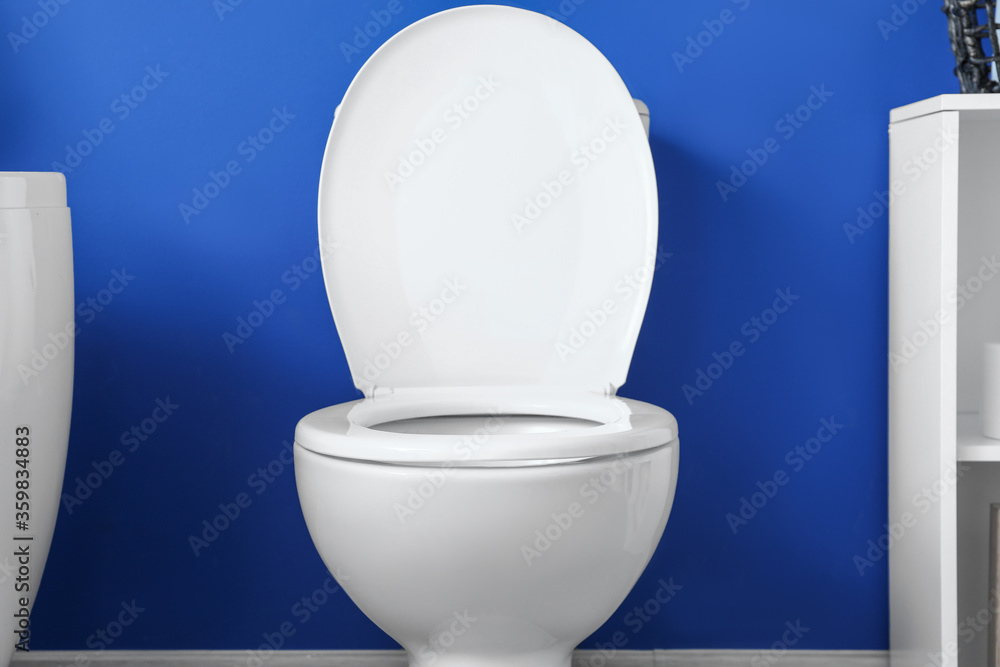 Modern toilet bowl near color wall in restroom