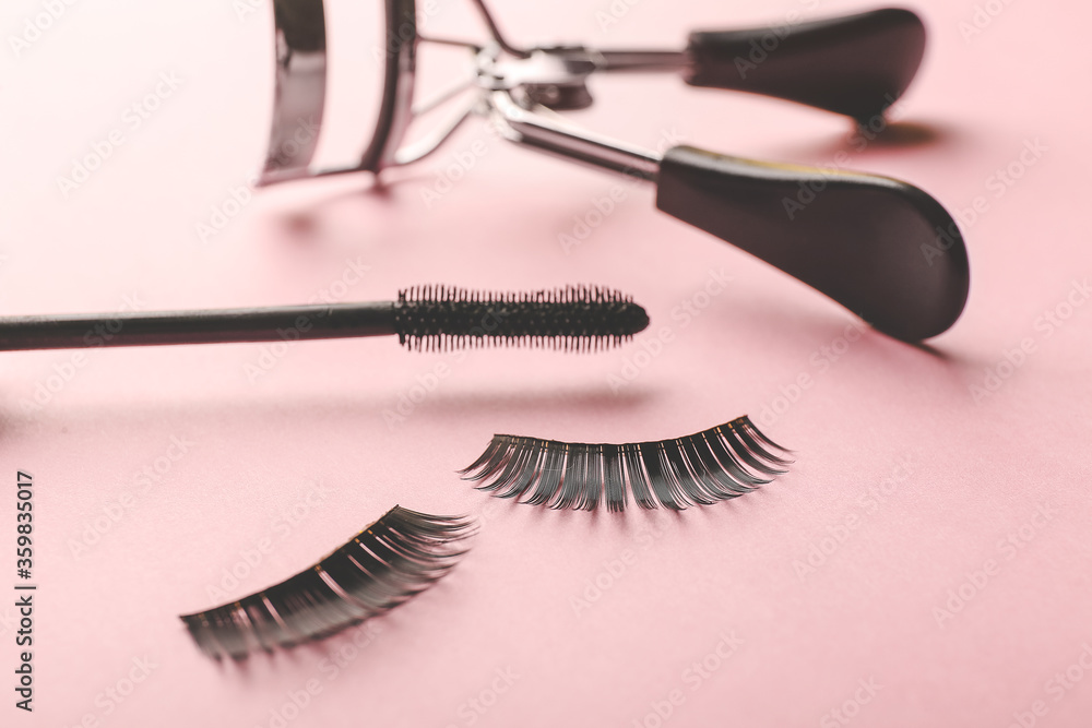 Black mascara, fake eyelashes and curler on color background