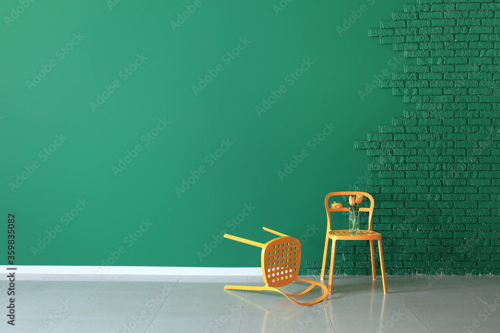 Chairs with bouquet of flowers near color wall in room