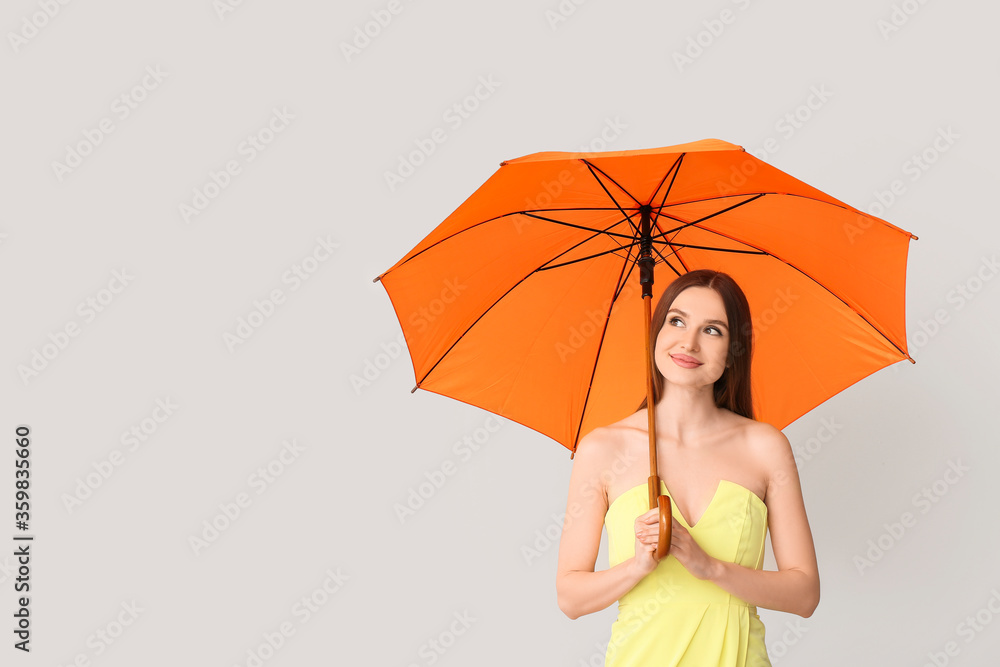 Beautiful woman with umbrella on light background