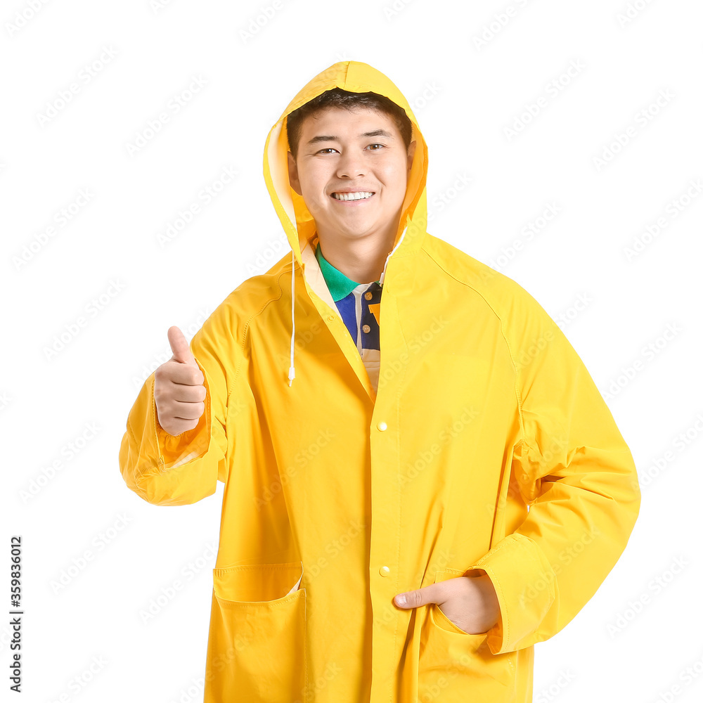 Young Asian man in raincoat showing thumb-up on white background