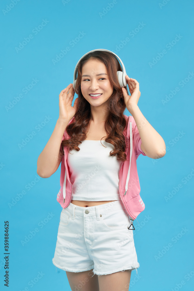 Adorable asian woman singing and having fun while listening to music using wireless earphones isolat