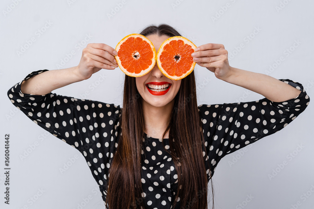 Cheerful girl holding grapefruit halves near eyes. Concept of crazy vegan person. Facial expressions