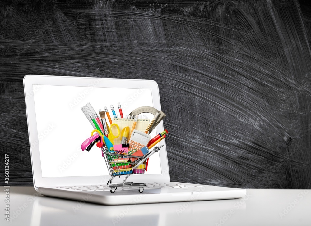 Stationery objects in mini supermarket cart and laptop on  desk