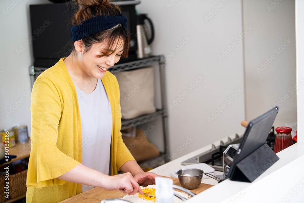 タブレットでレシピを確認しながら、小麦粉と卵を混ぜる調理中の女性