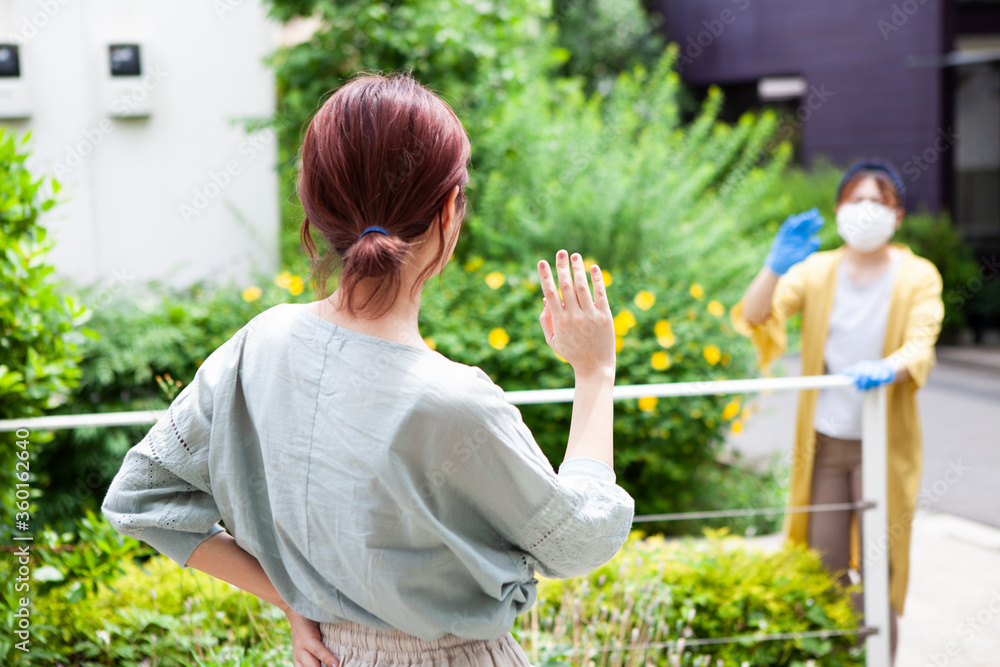 玄関の柵越しに家の中にいる友人に手を振る女性
